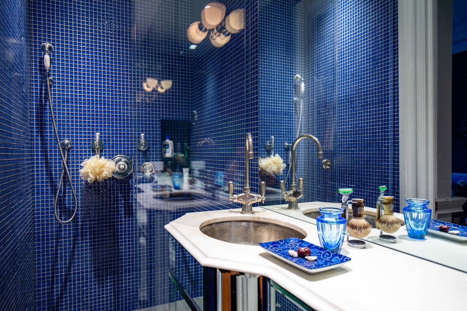 The blue walls in this bathroom perfectly match the water traditionally associated with blue. The yellow fixtures look great against blue wall backgrounds. The central elements of this composition - the countertops and the pedestal sink - are highlighted in white, which is considered universal. Indeed, white is in perfect harmony with both blue walls and yellow lamps. Dreaming of the perfect bathroom? Then elevate its interior design with our outstanding interior designers!